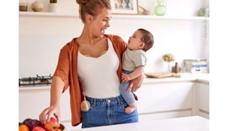 Mother holding child while in the kitchen, her hands are free to work while breast pump is active.